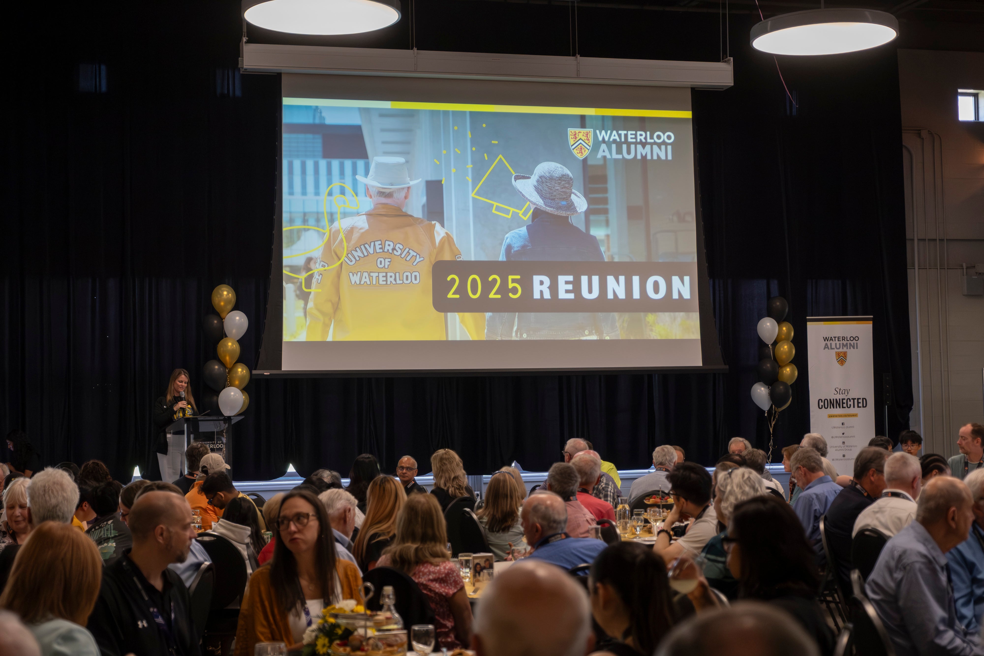 A group of people sit in front of a screen that reads 2025 Reunion