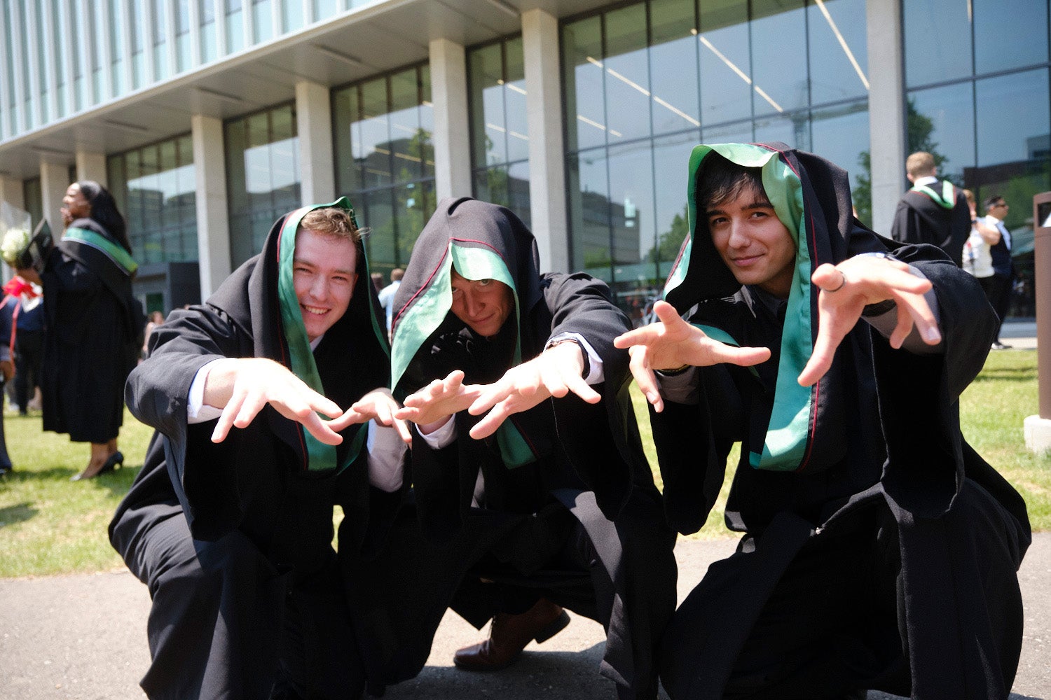 Three graduates with their hoods pulled over their heads wiggle their fingers at the camera