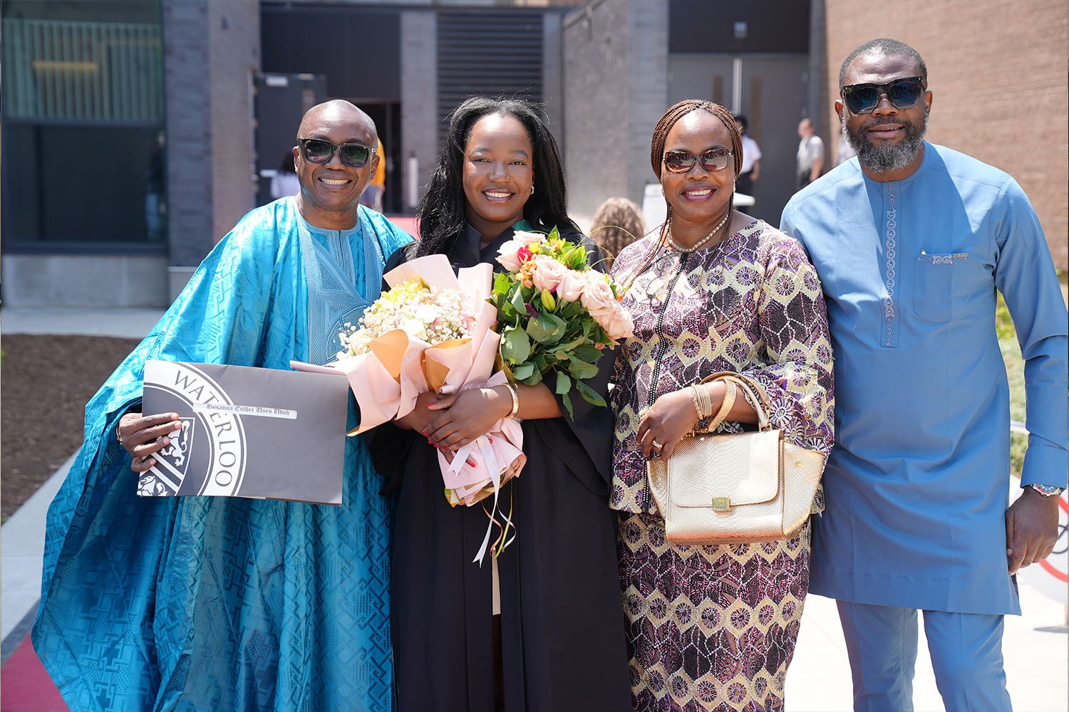 A graduate smiles with her family and holds two bouquets