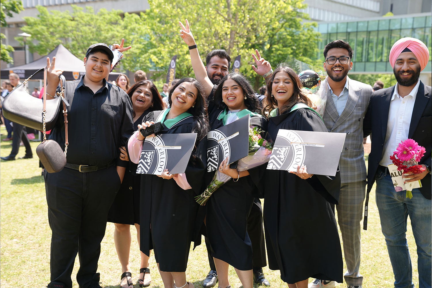 Eight friends smile, the front three holding up their diplomas
