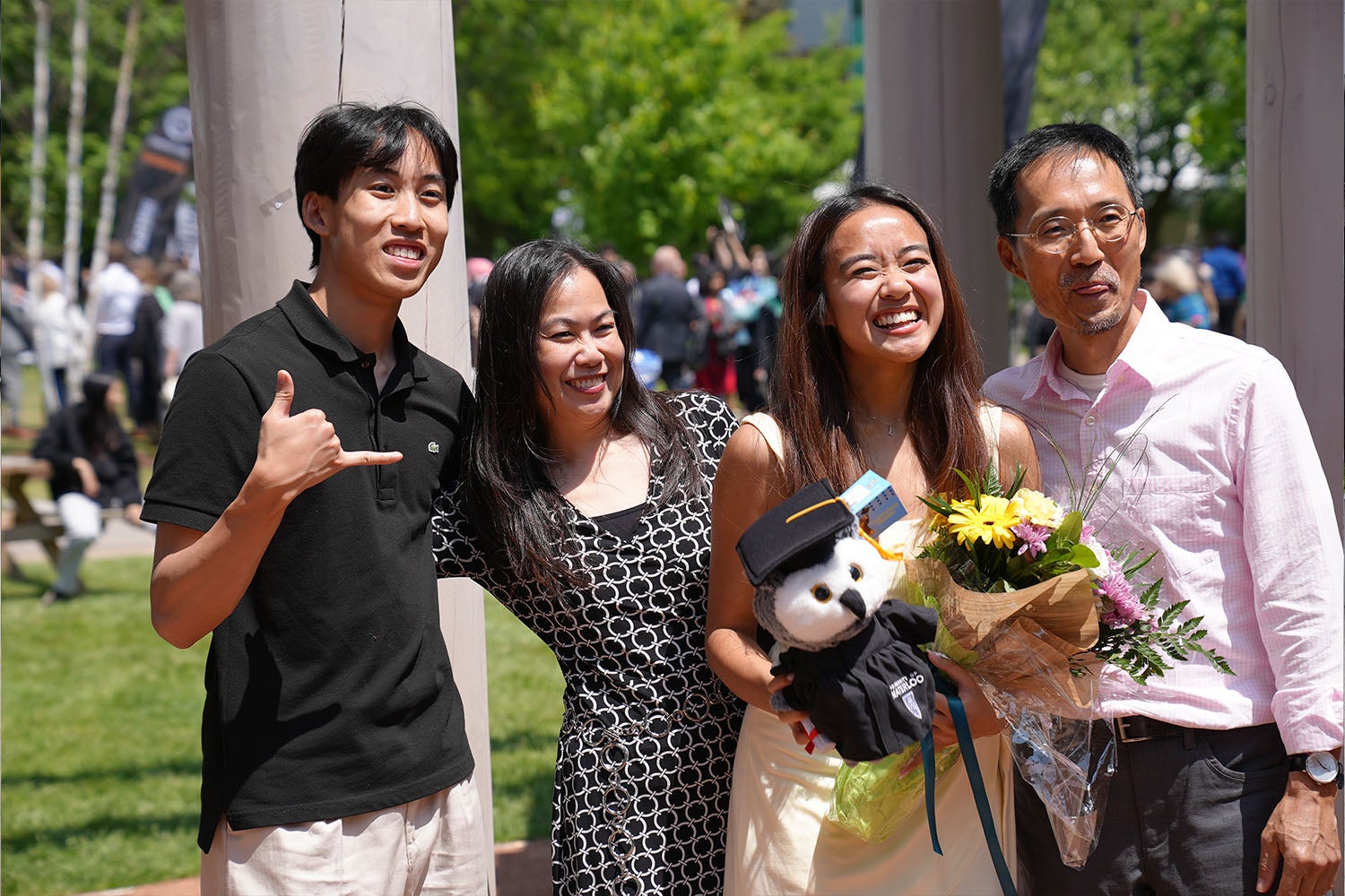 A graduate smiles with her family and holds a small teddy bear and flowers