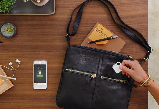 tile tracking device being put into a purse with iPhone beside it on a wooden desk