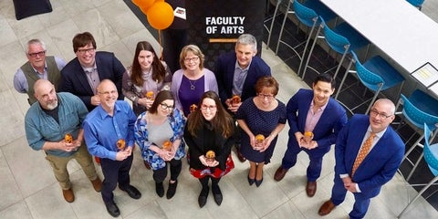 Group of faculty, staff and students smiling with award sculptures in their hands