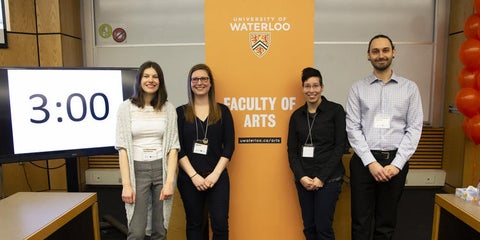 four 3MT winners smile in front of Arts banner