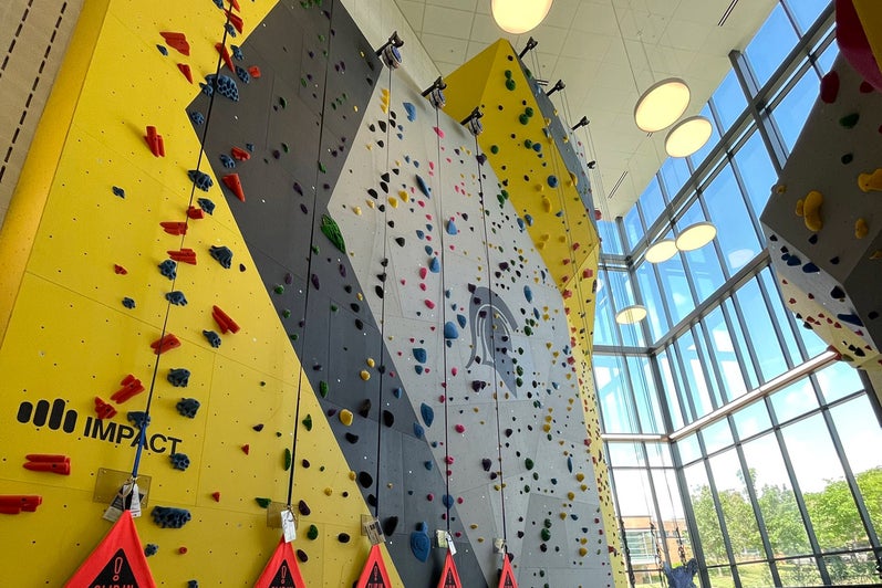 Porcellino standing by the climbing wall in the Physical Activities Complex.