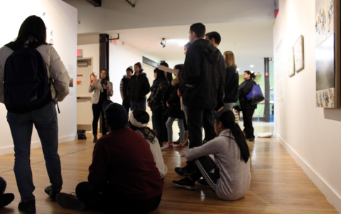 A group of students are gathered around art work hanging on a gallery wall