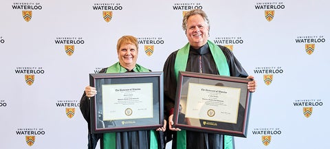 Maureen Jones and E. Paul Penner wearing convocation robes and holding up their framed certificates