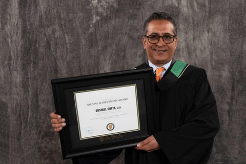 Susheel Gupta holding a frame with his Arts Alumni Achievement Award