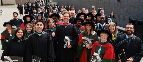 A group of new graduates in their gowns smile as they exit the PAC