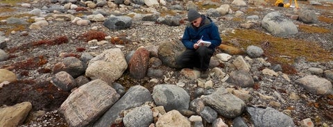 Douglas Stenton writing in notebook in rocky arctic landscape