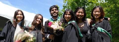 A group of new graduates in their convocation robes, holding flowers and smiling