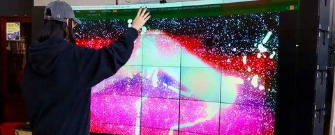Student moving arms in front of large colourful digital screen