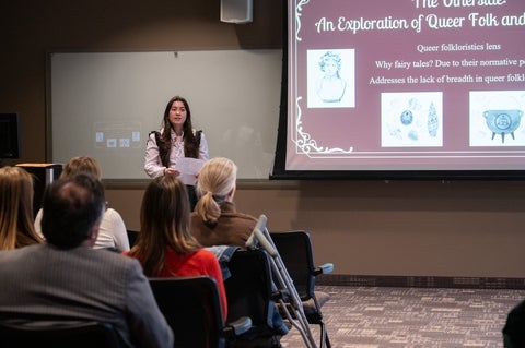 Student with slide on screen speaking to seated audience