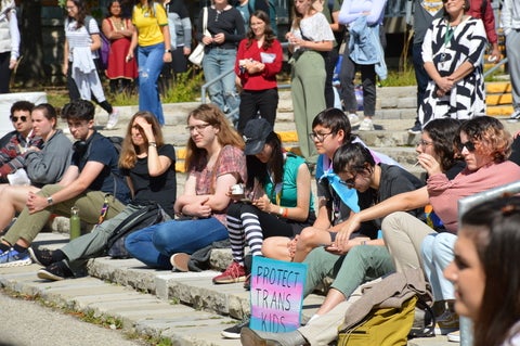 Students sitting on steps with signs supporting trans kids