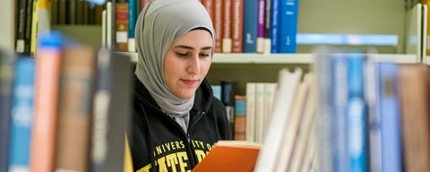 Student reading book in library stacks