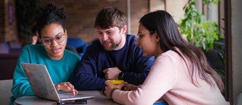 A group of graduate students huddle around a laptop in a student lounge