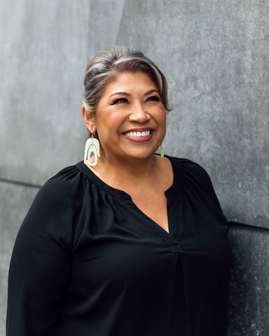 Kim Tallbear smiles in front of a concrete wall