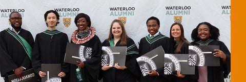 A group of Masters graduates hold up their diplomas infront of the Waterloo Alumni backdrop