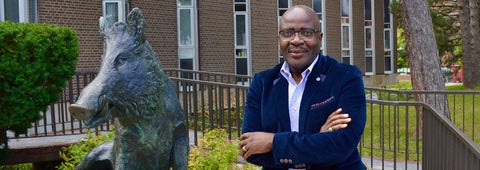 Dean Alexie Tchuyap standing next to the boar statue outside Modern Languages building