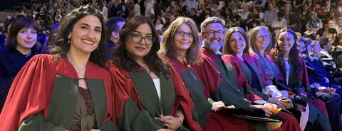 A row of new PhD graduates in the audience at Convocation, wearing their red and green academic robes