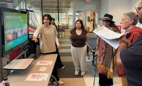 Student presenting design concepts on large digital screen to several people