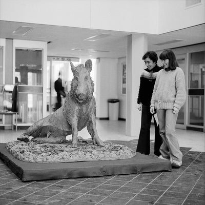 Black and white photo of two students looking at Porcellino's statue in the ML lobby