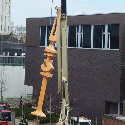 A crane lifts the yellow structure shaped like a fork