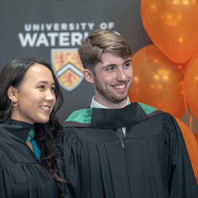 Two graduates pose with orange balloons