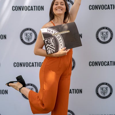 Grad wearing an orange jumpsuit jumping in the air in celebration