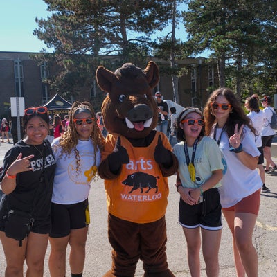 four smiling students in orange sunglasses with boar mascot