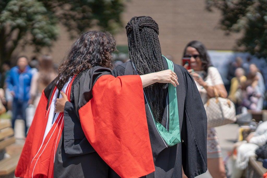 Two graduates pose for a photo wearing their full academic regalia