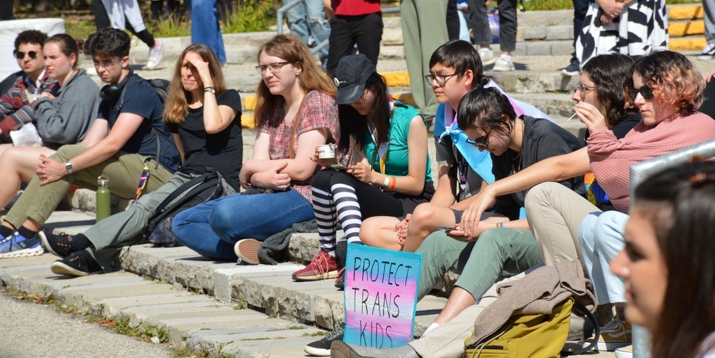 Students sitting on steps with signs supporting trans kids