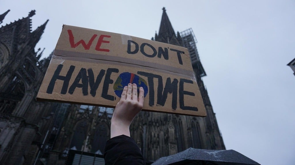 Protester holding up cardboard sign that says "we don't have time"