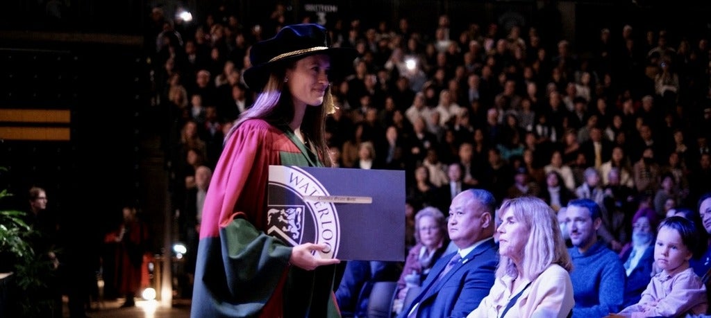 Woman in doctoral regalia holds diploma
