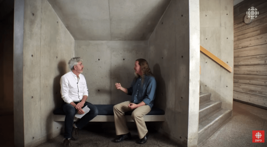 two men sitting on bench inside a building talking