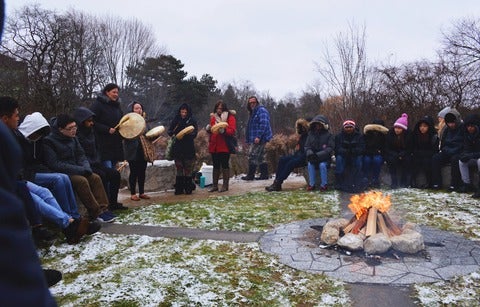 people gathered around ceremonial fire with drummers and singers