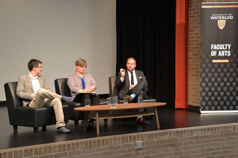 three professors in chairs on stage at event