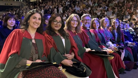 A row of PhD students in the audience at convocation, all wearing their bright red and green robes