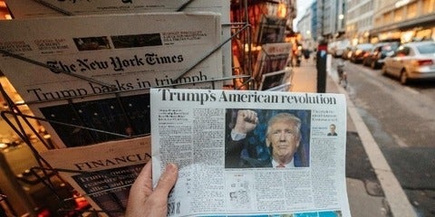 person's hand holding paper with headlines about Trump