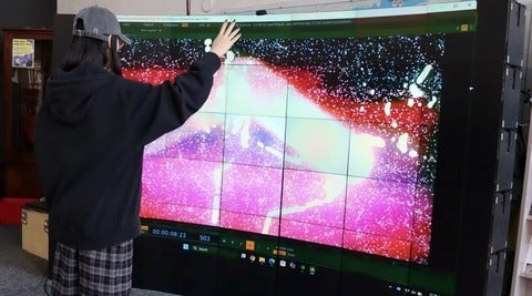 Person making arm gestures in front or large colourful digital screen