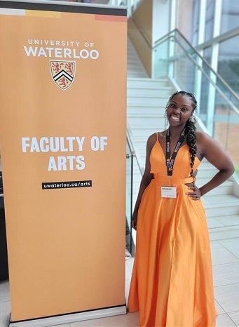 Emily Radcliffe posing beside a Faculty of Arts banner