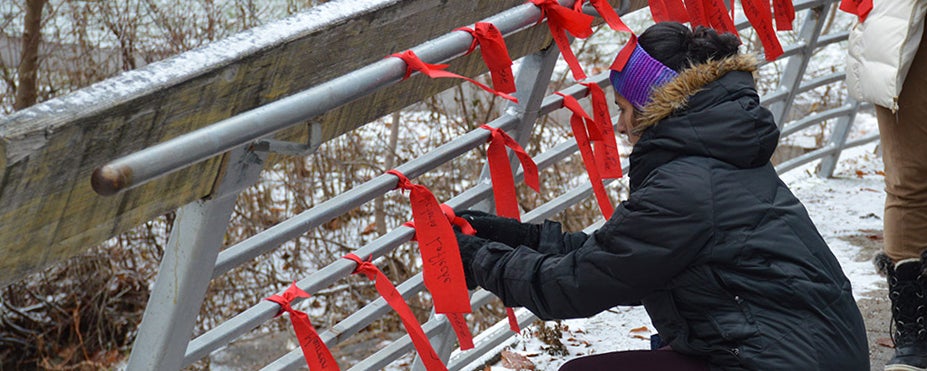 woman tying red cloth strips to bridge railing