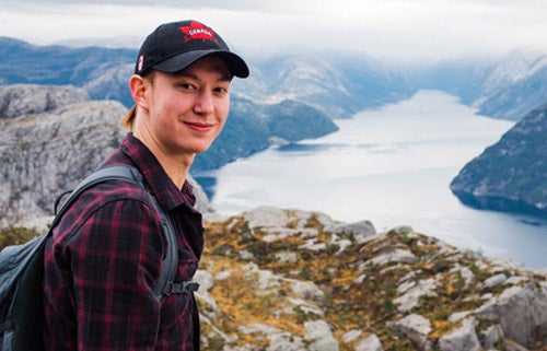 A male student over looks a neautiful landscape a river cutting through snow topped mountains