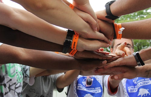 Arts students at orientation wearing orange bracelets clasp hands to show solidatiry to the group