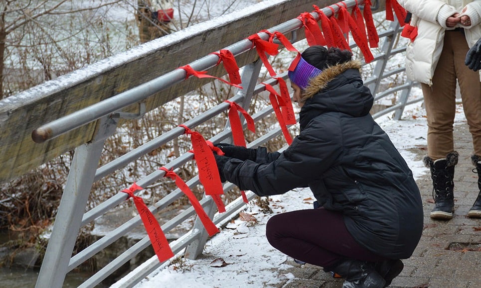 woman tying red ribbons to bridge railing