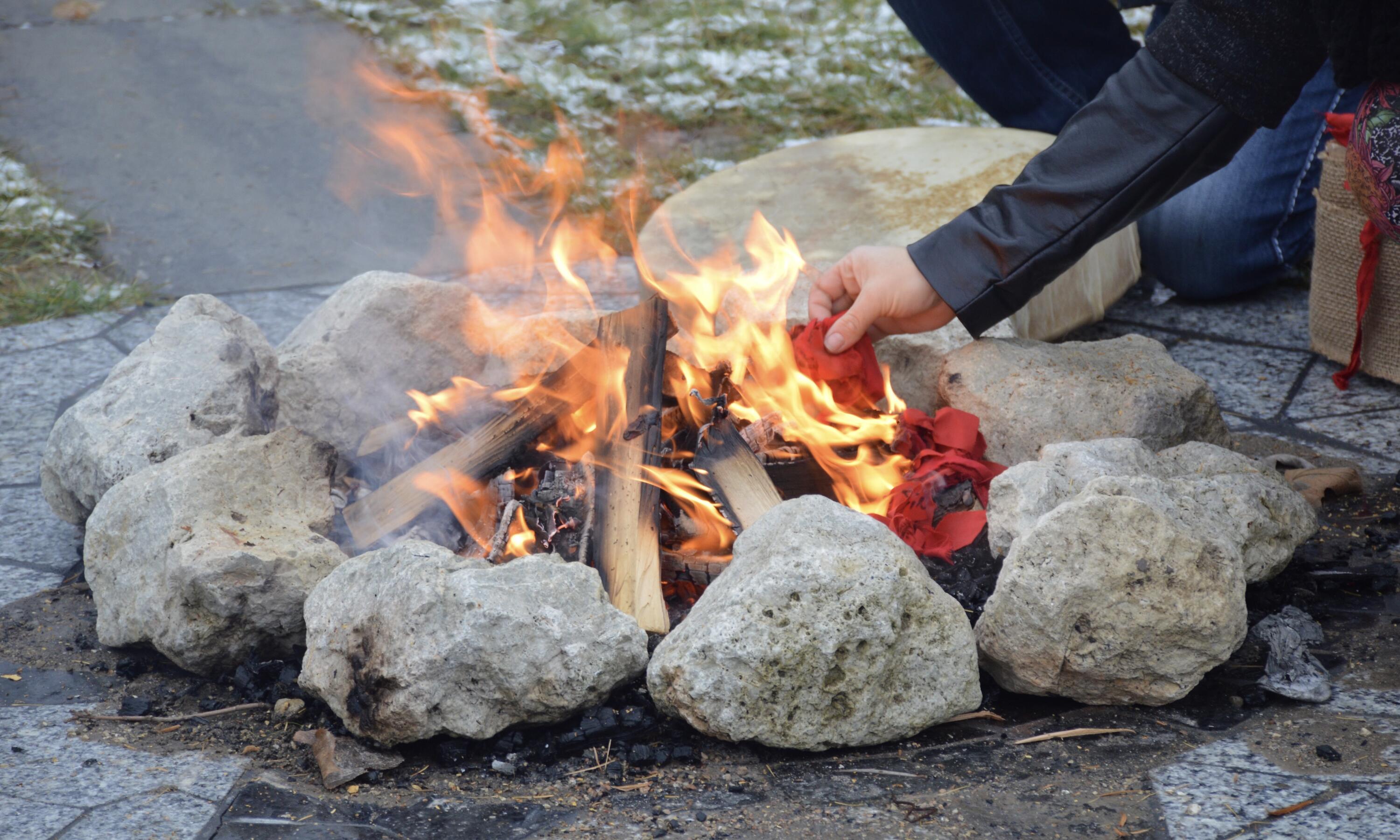 hand adding red ribbons to ceremonial fire