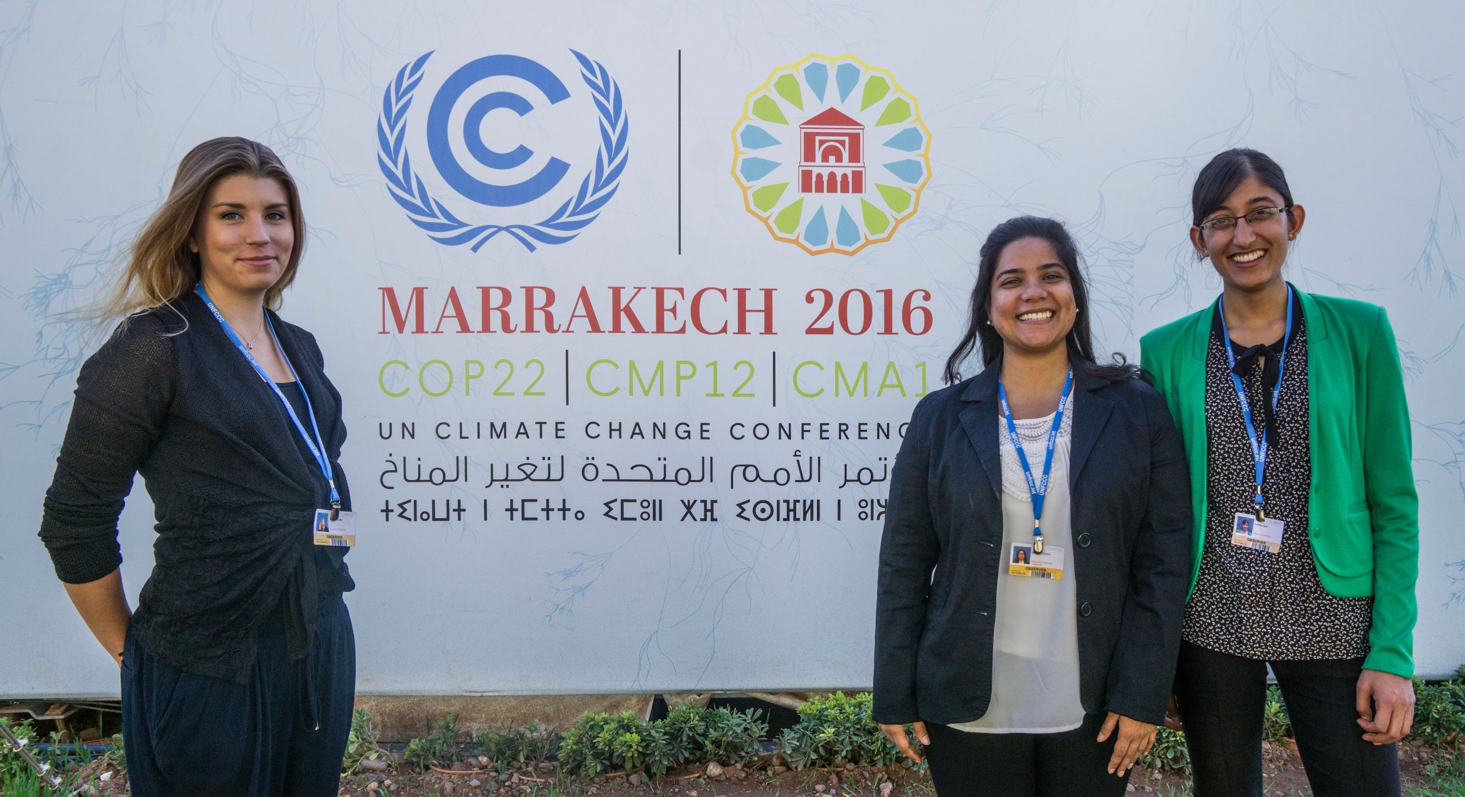 three women smile in front of COP22 sign