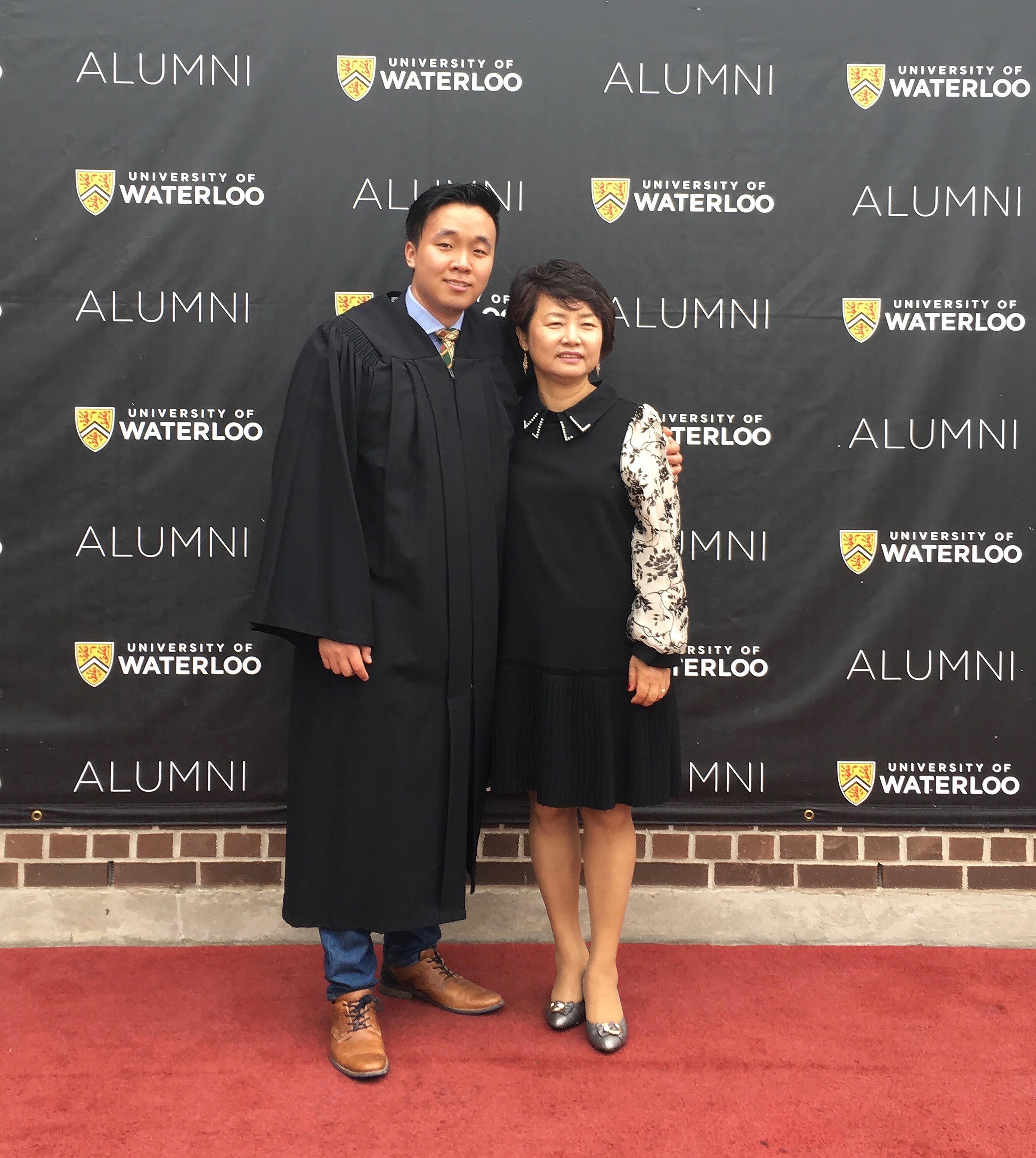 David and his mom posing in front of a banner at convocation