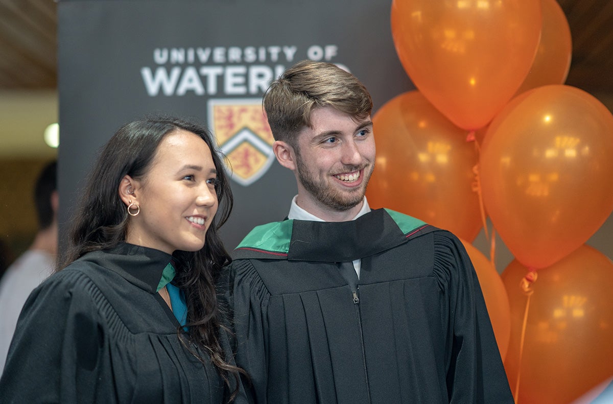 Two graduates pose with orange balloons
