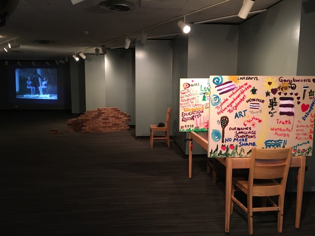 A gallery space with different pieces of art, including poster boards, part of a brick wall, and a project photograph in the background